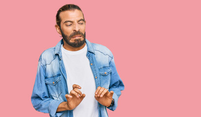 Attractive man with long hair and beard wearing casual denim jacket disgusted expression, displeased and fearful doing disgust face because aversion reaction.