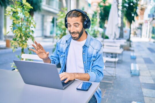 Young middle eastern man doing video call using laptop and headphones at coffee shop terrace.