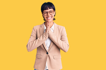 Young brunette woman with short hair wearing business jacket and glasses praying with hands together asking for forgiveness smiling confident.