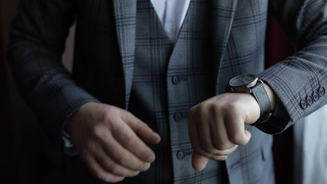 Young man in suit put on wrist watch. Groom dresses. Handsome male businessman is waiting for a meeting. Hand with a clock close up. Waits. Looks at the clock, time. Wristwatch on man arm. Slow motion