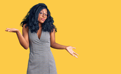 Beautiful african american woman wearing business dress and glasses clueless and confused expression with arms and hands raised. doubt concept.