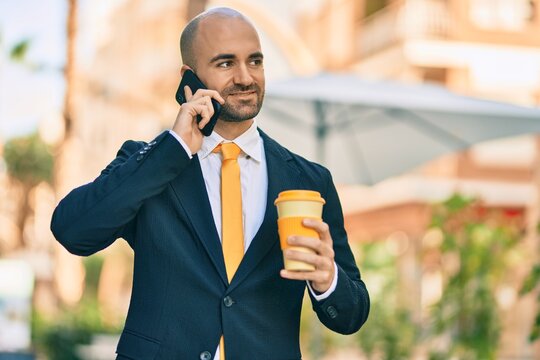 Young hispanic bald businessman talking on the smartphone drinking coffee at the city.