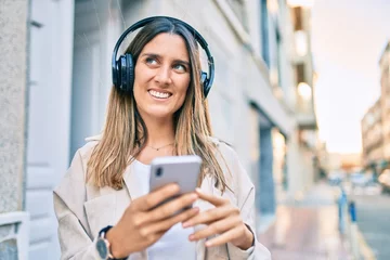 Foto op Plexiglas Young caucasian woman smiling happy using smartphone and headphones at the city. © Krakenimages.com