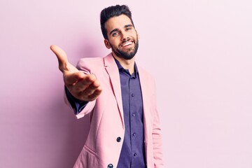 Young handsome man with beard wearing elegant jacket smiling friendly offering handshake as greeting and welcoming. successful business.