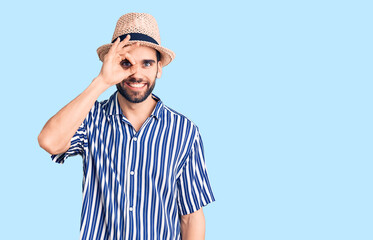 Young handsome man with beard wearing summer hat and striped shirt doing ok gesture with hand smiling, eye looking through fingers with happy face.