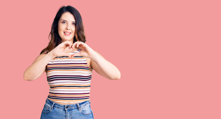 Beautiful young brunette woman wearing casual clothes smiling in love showing heart symbol and shape with hands. romantic concept.