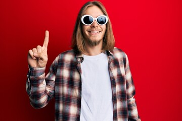 Handsome caucasian man with long hair wearing hipster shirt wearing sunglasses smiling with an idea or question pointing finger up with happy face, number one