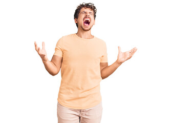 Young handsome man with curly hair wearing casual clothes crazy and mad shouting and yelling with aggressive expression and arms raised. frustration concept.