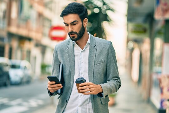Young hispanic businessman with serious expression using smartphone and drinking coffee at the city.