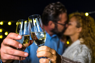 close up of hands of two happy and in love people holding their glass with champagne and kissing at the background for the new year 2021