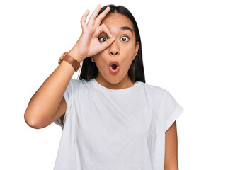 Young asian woman wearing casual white t shirt doing ok gesture shocked with surprised face, eye looking through fingers. unbelieving expression.