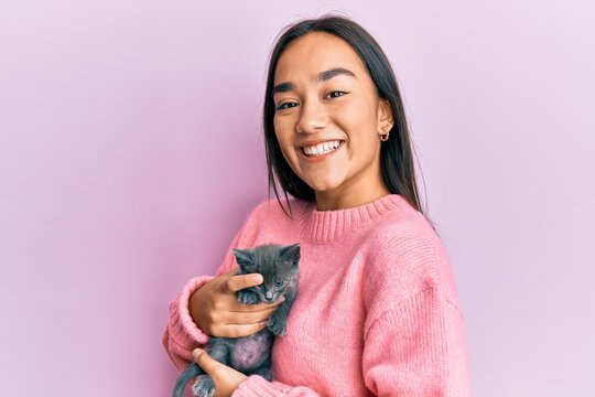 Young hispanic girl smiling happy holding cute cat over isolated pink background.
