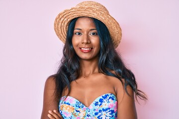 Young indian girl wearing bikini and summer hat happy face smiling with crossed arms looking at the camera. positive person.