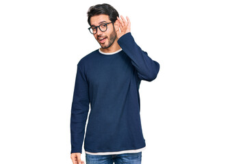 Fototapeta premium Young hispanic man wearing casual clothes and glasses smiling with hand over ear listening an hearing to rumor or gossip. deafness concept.
