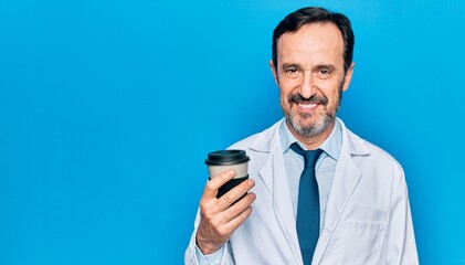 Middle age handsome doctor man wearing coat drinking cup of takeaway coffee looking positive and happy standing and smiling with a confident smile showing teeth