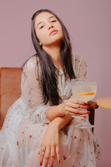 Young woman with glass of cocktail in hand. Studio photo with pink background.