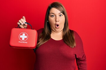 Beautiful hispanic plus size woman holding first aid kit smiling with an idea or question pointing...