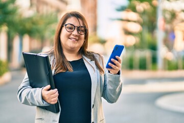Young plus size businesswoman using smartphone holding binder at the city