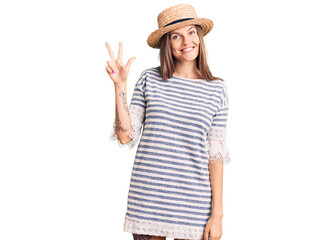 Obraz na płótnie Canvas Beautiful caucasian woman wearing summer hat showing and pointing up with fingers number three while smiling confident and happy.