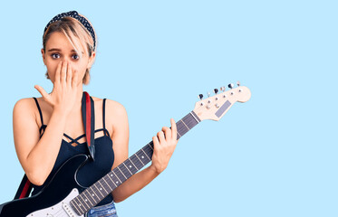 Young beautiful blonde woman playing electric guitar covering mouth with hand, shocked and afraid for mistake. surprised expression