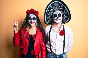 Plakat Couple wearing day of the dead costume over yellow showing and pointing up with fingers number two while smiling confident and happy.