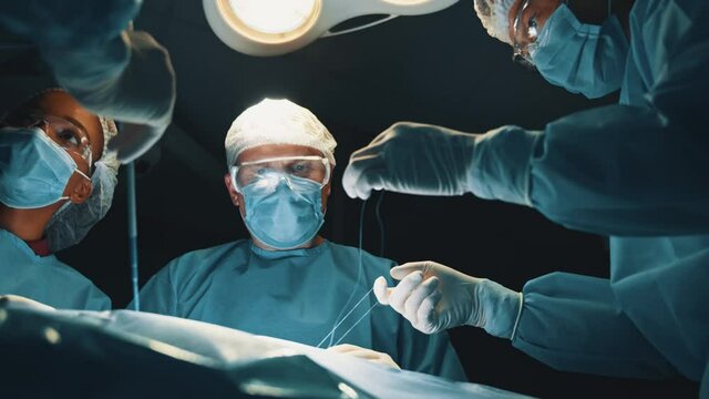 Caucasian skillful surgeon with group of medical multi-race workers performing surgical operation in operating room of modern hospital.