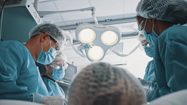 Multi-race team of professional surgeon and younger doctors performing plastic surgery treatment for female patient. Surgical staff. Hospitals.