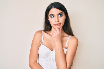 Naklejka premium Brunette teenager girl posing elegant with hand on chin thinking about question, pensive expression. smiling with thoughtful face. doubt concept.
