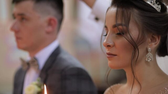 Newlyweds. Elegant caucasian bride and the groom stand in church at christianity wedding ceremony, holding candles in their hands. The wedding matrimony of the man and woman. Slow motion, close up