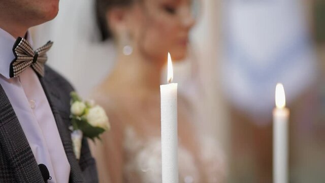 Newlyweds. Elegant caucasian bride and the groom stand in church at christianity wedding ceremony, holding candles in their hands. The wedding matrimony of the man and woman. Slow motion, close up