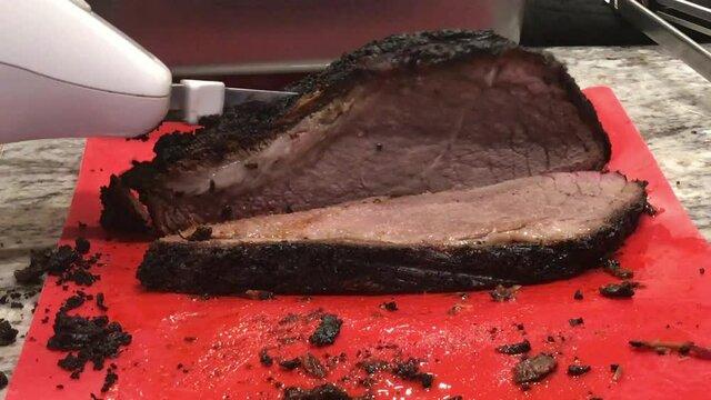Electric knife cutting hot steaming beef barbecue brisket