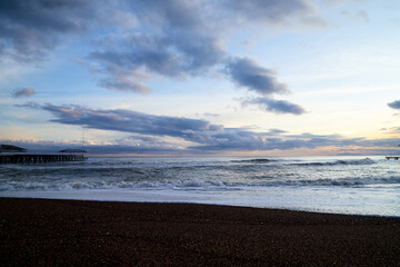 View from beach to water of sea, waves with white foam, pierce and sky with clouds in a nice evening.