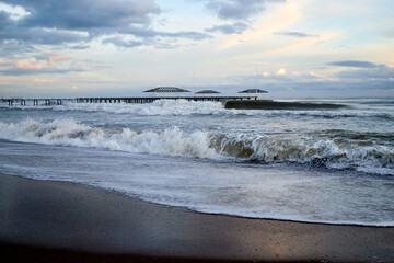 View from beach to water of sea, waves with white foam, pierce and sky with clouds in a nice evening.