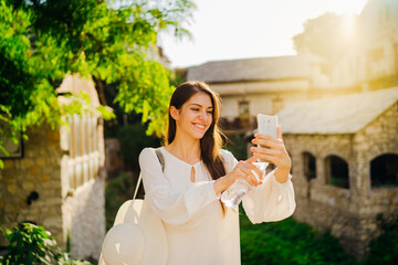 Smiling young tourist making selfie with smartphone in front of historic landmark in old town in...