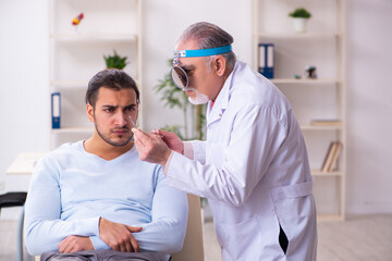 Obraz premium Young sick man visiting old doctor otolaryngologist