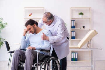 Young man in wheel-chair and old doctor traumatologist