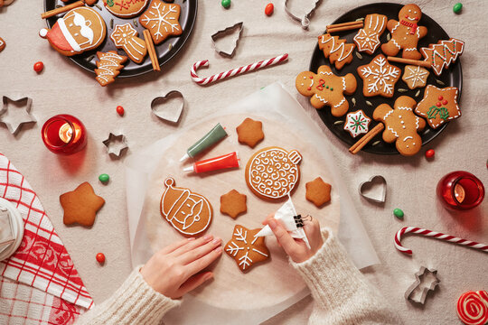 Woman's hands decorating a traditional gingerbread. Xmas flat lay. Christmas and New Year holidays mood. Top view of home table.