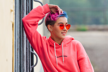 Portrait of a young girl with short colorful hair and nose piercing satanding near the wall with...