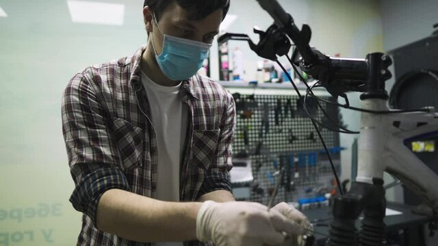 Service engineer performs diagnostics and repairs on bicycle in professional workshop, wearing protective mask and safety gloves from client covid 19. Service topic during coronavirus pandemic