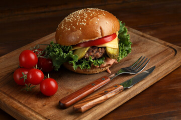burger on a dark wooden table with tomatoes and cutlery