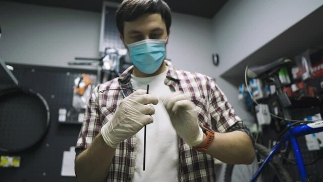 Bicycle mechanic repairs and maintains customer bike in accordance with quarantine standards during coronavirus pandemic, wear medical mask and gloves. Individual transport during lockdown covid 19