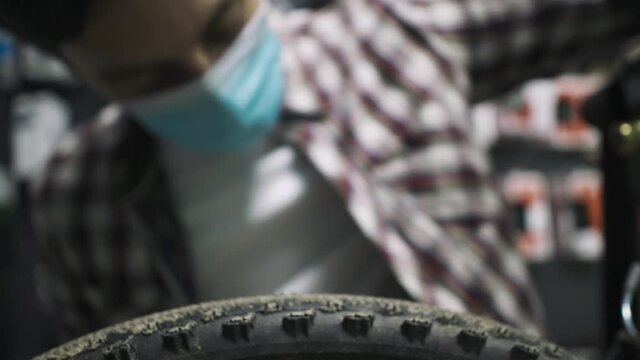 Theme service maintenance and repair of bike in bicycle store during coronavirus epidemic. Mechanic repairs mountain cycle wearing protective mask, new rules covid 19. Subject workman profession