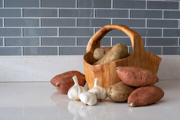 carved wooden basket with russet potatoes, sweet potatoes and garlic
