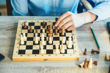 Teenager plays chess. Boy makes move with a figure on wooden chessboard. Hobby, leisure concept