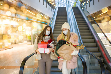 Young women in medical mask shopping for Christmas in mall. Xmas holidays in new Covid-19 reality. Selective focus