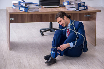 Fototapeta na wymiar Chained male employee unhappy with excessive work in the office