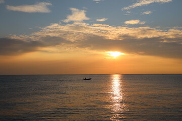 Obraz premium Orange Sunset at dawn with the wide view of sea and small boat floating on the ocean