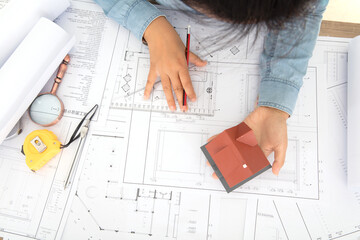Looking down and shooting, the hard-working architect is holding a small house model and working...