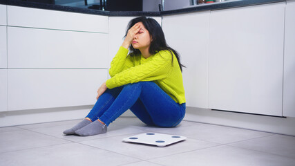 Frustrated dieting young asian woman sitting on the flor with weight scale in front. Weight loss...