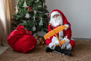 Santa Claus is tired. Santa sits on the floor with a bag of gifts and plays with a toy airplane. He...